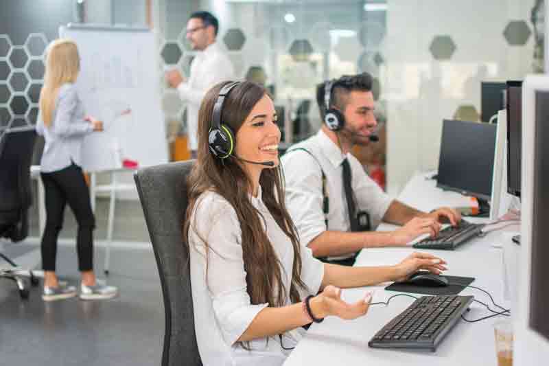 Zentraler Kundendienst, TANTZKY Service-Center, lachende Frau mit Headset, fröhlicher Mann mit Headset im Vordergrund, Hintergrund Mann und Frau an Flipchart 