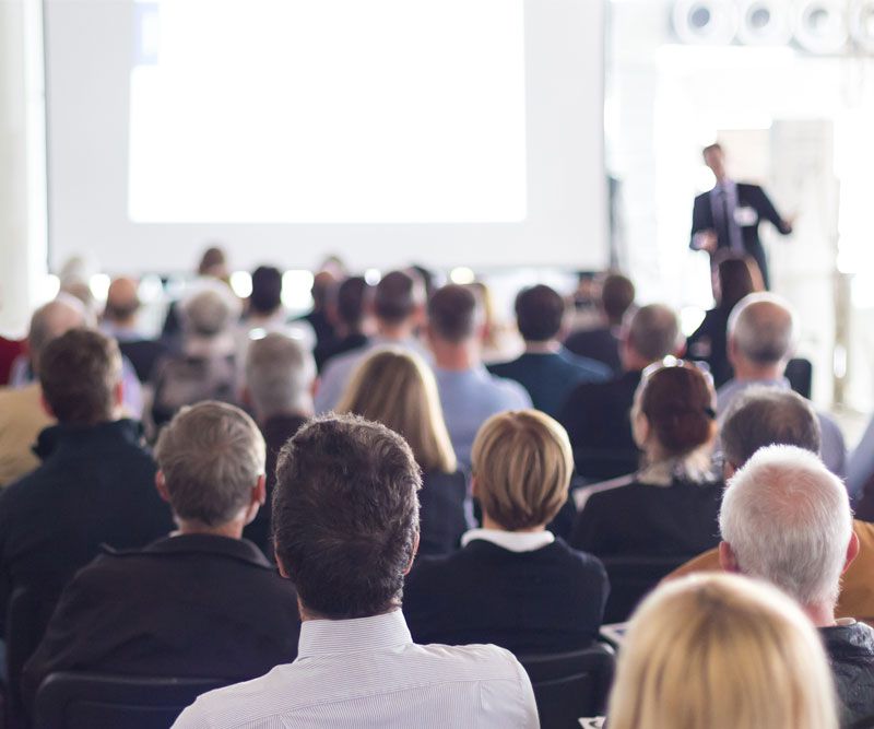 Im Vordergrund viele Menschen mit Blick nach vorn zur Präsentation